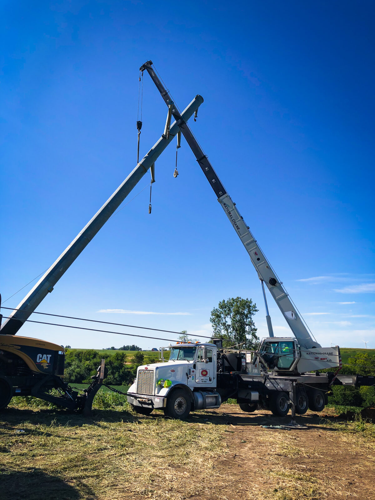 Crane truck in green farming filed with boom lifting transmission pole